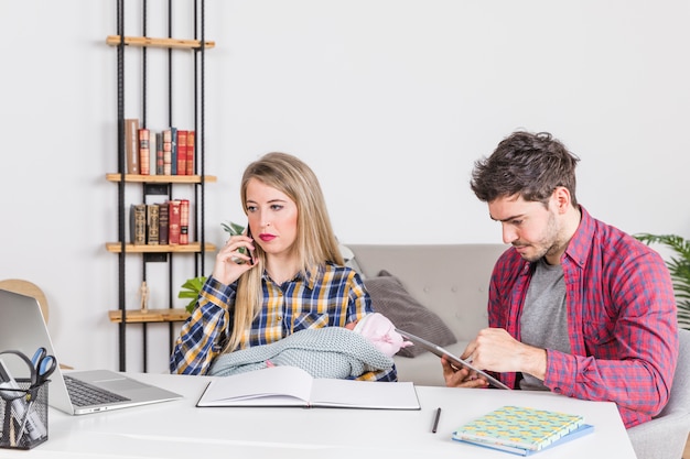 Mother with baby talking on phone while father using tablet